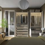 Modern bedroom with a large open closet, featuring hangers, shelves, and storage baskets. A green bed and a white pendant light are visible.