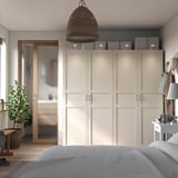 Modern bedroom with beige PAX wardrobe, grey rug, wicker pendant light, white bed, wooden floor, and houseplant.