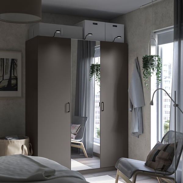 Modern bedroom with large mirrored PAX wardrobe reflecting a chair, featuring sleek handles and integrated lighting.
