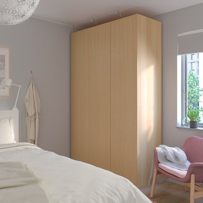 Large wooden PAX wardrobe against wall, with coat hooks, chair, bed, and window.