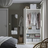A modern bedroom an open white PAX wardrobe displaying clothes, folded sweaters, and storage boxes, with narrow frames suitable for small spaces.