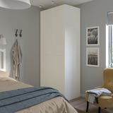 Modern bedroom with white PAX wardrobe, bed, art, and yellow chair.