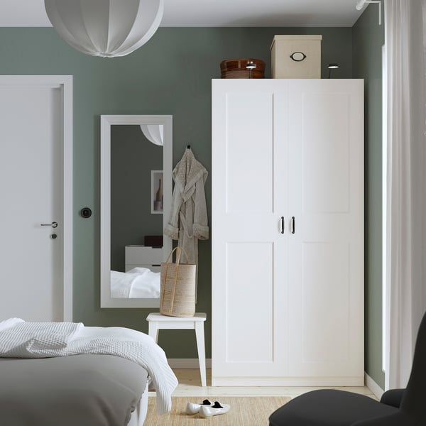 Modern bedroom with tall white PAX wardrobe, black handles, decorative boxes, mirror, wicker basket, and hanging lamp.