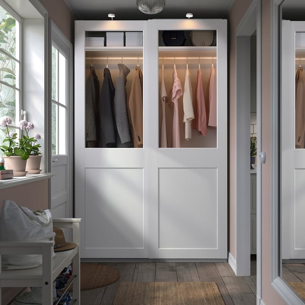 White PAX wardrobe with glass doors, clothes, and plants.