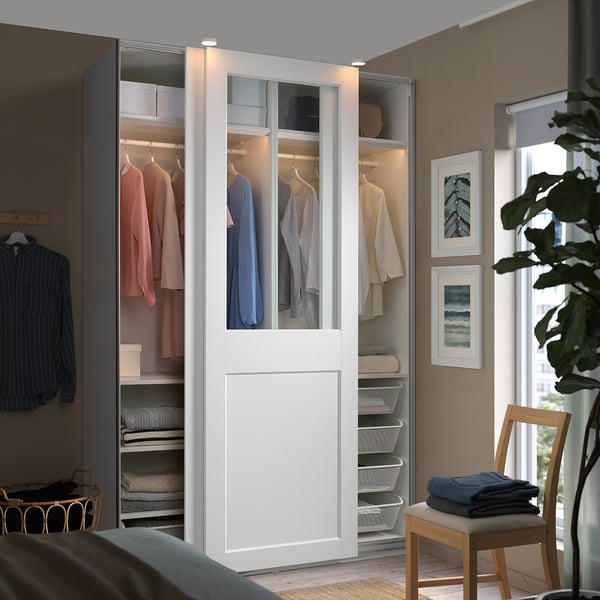 Modern white PAX wardrobe with glass doors, showing organized clothes and accessories.