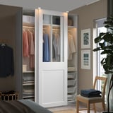 Modern white PAX wardrobe with glass doors, showing organized clothes and accessories.