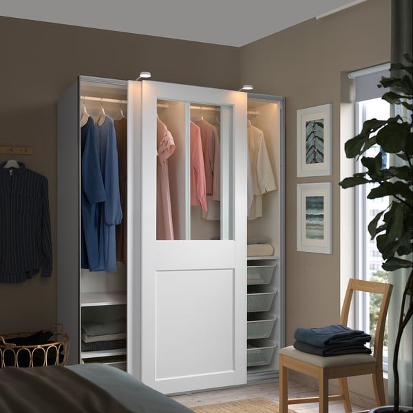 A large, white, modern PAX wardrobe with glass doors, neatly storing a variety of clothing items and accessories.