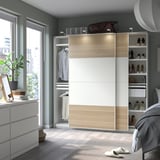 Modern bedroom with white and light wood PAX wardrobe, open to show clothes and shoes, next to a window.