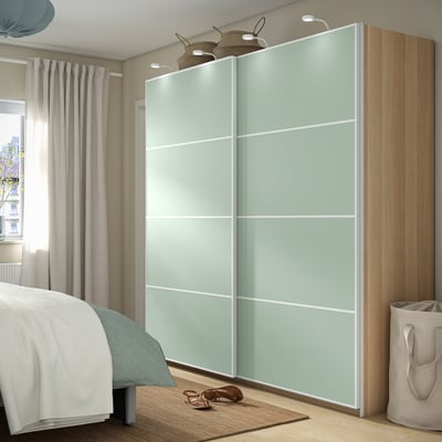 Bedroom with PAX: tall light green sliding closet, wooden side panel, bed, curtains, and sandals.