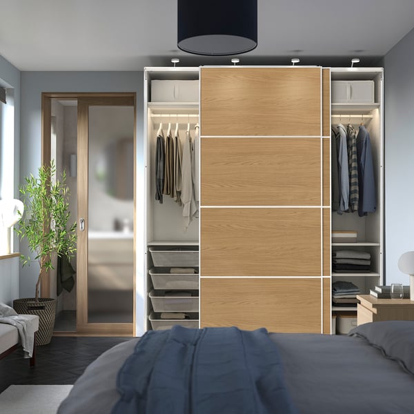 Modern bedroom with open wardrobe showcasing hanging clothes, folded items, and sliding doors.