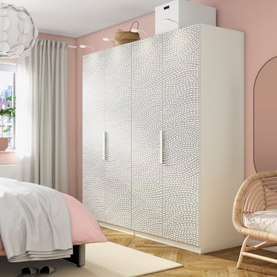 Stylish bedroom with white dotted PAX wardrobe, double doors, and mesh baskets. Central piece between bed, wicker chair, and large mirror.