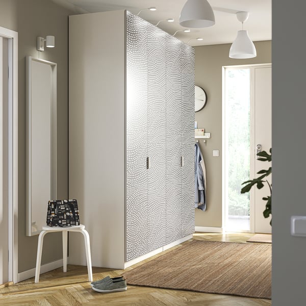 Modern entryway with wavy-patterned white PAX wardrobe, stool, rug, and glass door.