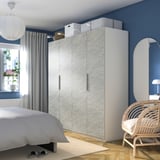 Minimalist bedroom: large light gray textured PAX wardrobe & white wicker chair against dark blue wall.