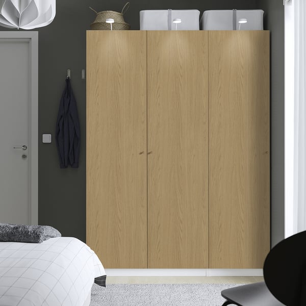 Large light wooden PAX wardrobe fits well in bedroom, with three sections, clothes hangers visible. Top boxes and hat added storage.