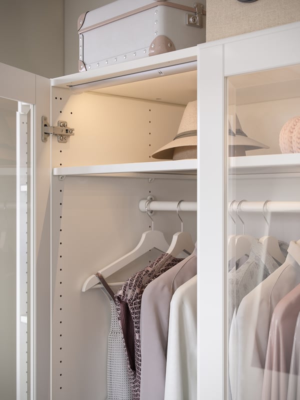PAX white closet stores clothes, hats in organized shelves and hanging racks.