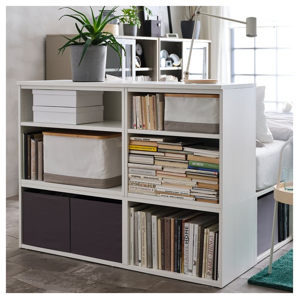 A white PLATSA bookshelf, holding books and a plant.