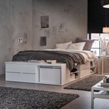 Modern bedroom with PLATSA bed, white, on castors, grey bedding, storage under bed, grey rug, artwork on walls.