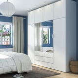 Modern bedroom with white PLATSA storage, mirrored doors, checkered bed, grey drapes, wicker basket.