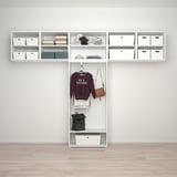 Organized closet with shelves holding white boxes and accessories, featuring a hanging area with a maroon sweatshirt, handbag, and green backpack.