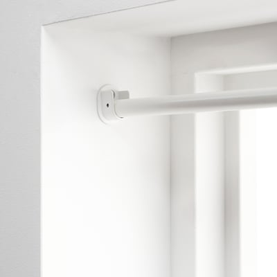 White adjustable curtain rod mounted on wall, part of IKEAs racka series, designed to extend across the entire wall for edge-to-edge privacy.