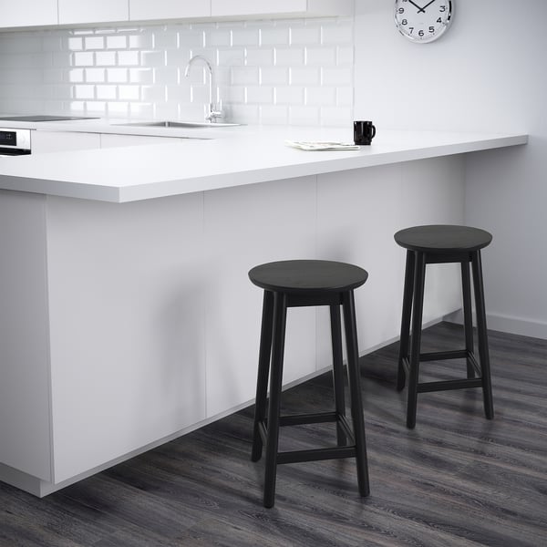 Black bar stools at white kitchen island with sink, backsplash, and clock.