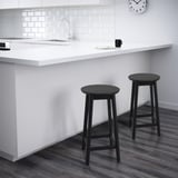 Black bar stools at white kitchen island with sink, backsplash, and clock.