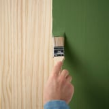 Painting a wooden surface with a green hue. A paintbrush held by a hand applies paint, transforming the woods color.