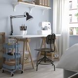 Small blue RÅSKOG trolley under desk, holding containers with craft supplies. Steel, rectangular, with four wheels, fits under desk.