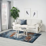 Modern living room with white sofa, abstract rug, and tall plant. Artwork and coffee table on rug.