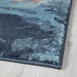 Soft, textured carpet corner, varying shades of blue, on light wooden floor.