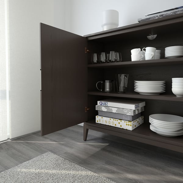 Open wooden cabinet showing dishes, glasses, mugs, and game boxes arranged on shelves.