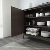 Open wooden cabinet showing dishes, glasses, mugs, and game boxes arranged on shelves.