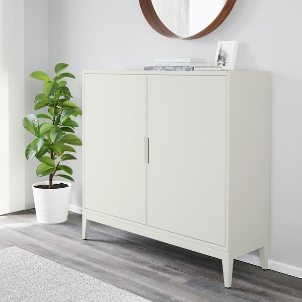 White cabinet with two doors and adjustable shelves. Houseplant beside it. Mirror above cabinet.