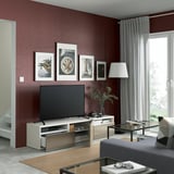 Modern living room with burgundy walls, flat screen tv, storage console, grey sofa, glass coffee table, and large window with curtains.