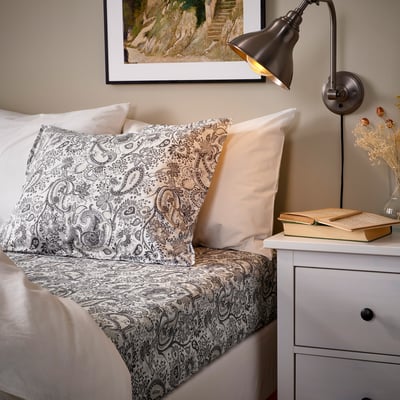 Bed with paisley pillows and blanket, white decor, cozy ambiance.