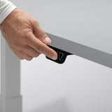 Person adjusting height of electric standing desk with touch control button.