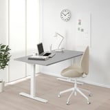 Modern office with adjustable RODULF desk near window, chair, laptop, keyboard, lamp.