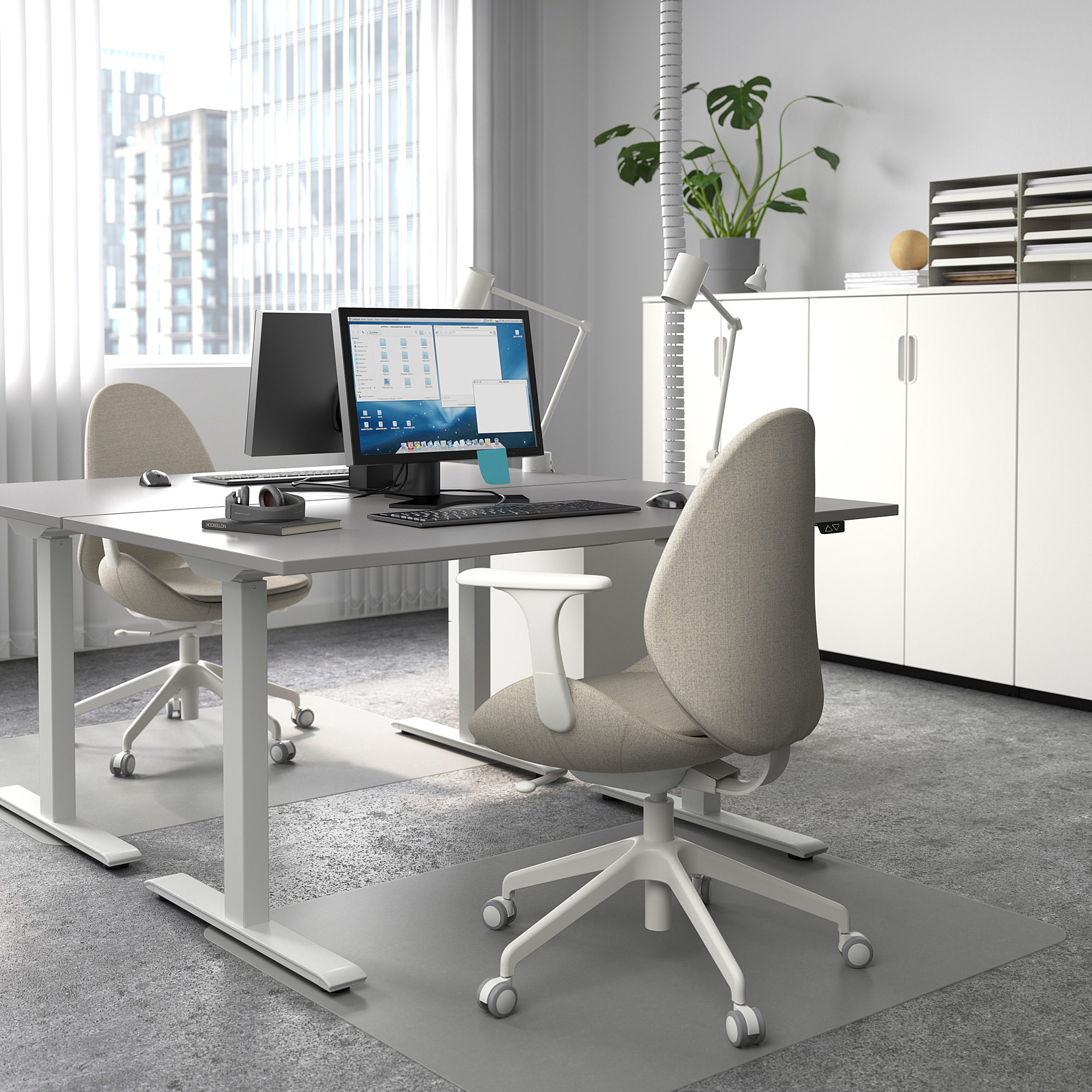 Modern sit-stand desk in office with two monitors, laptop, ergonomic chairs, and city view.