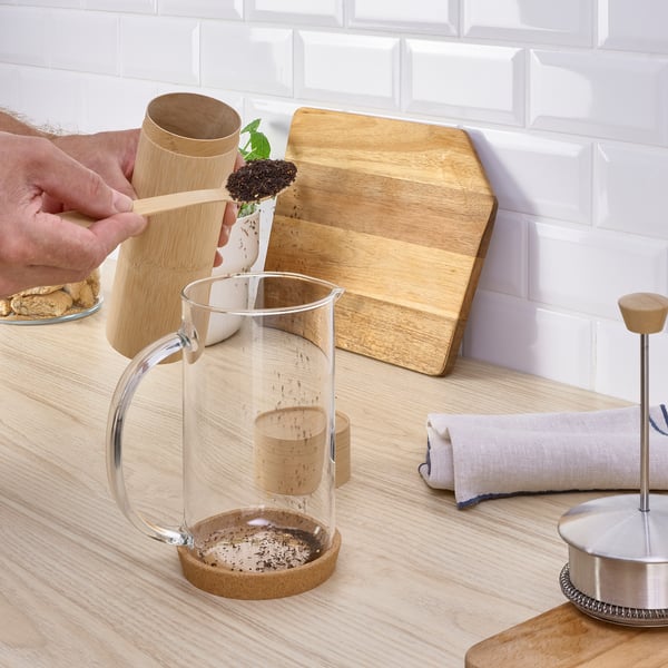 Adding coffee grounds to glass jar on wooden counter