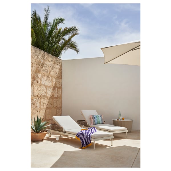 Modern outdoor lounging area with white SEGERÖN recliners, striped towel, side table, and palm tree.