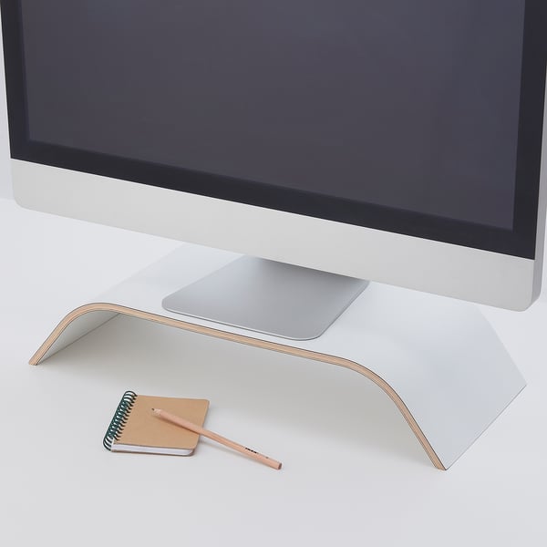 A monitor stand with a laptop, holding a monitor at an ergonomic height. Below it, a notepad and pencil show accessible storage.