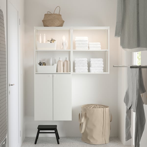 Modern bathroom with white wall unit and black stool. Laundry basket below, towels and bottles on shelves.