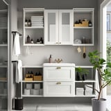 Organized modern bathroom with white cabinets, glass doors, and a sink. A plant on a shelf beside the sink.
