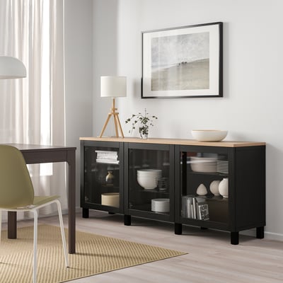 Black-brown SINDVIK cabinet with glass doors, showcasing dishes and books under a beach photo.