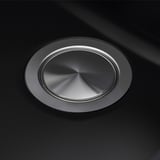 Round stainless steel sink drain cover on black sink. High-quality, reflective surface with smooth finish. Centered, polished metallic design.