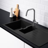 Modern kitchen sink with integrated drainboard. Silver faucet, black countertop, and white-tiled wall.
