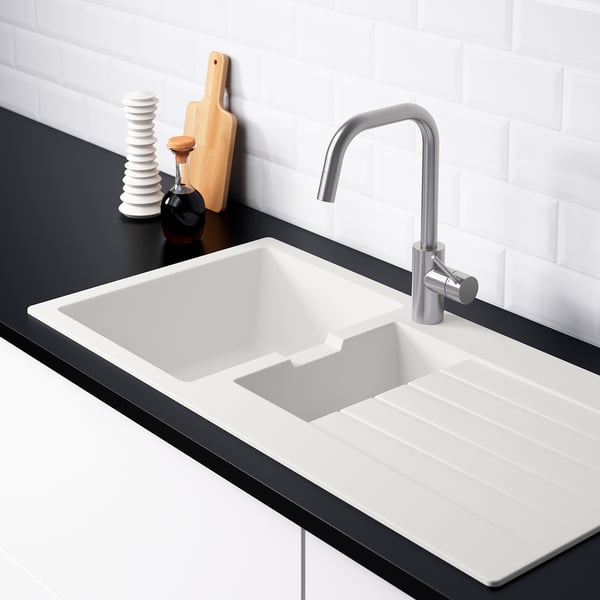 Modern kitchen sink with reversible drainboard, sloping water flow, two tap holes, white, black countertop, silver faucet, wooden cutting board.