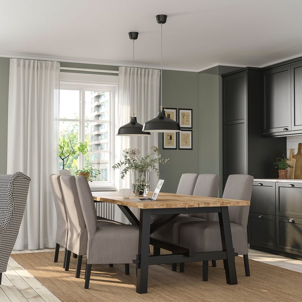 Modern dining area with SKOGSTA table and gray chairs, black pendant lights, green wall, and large window with white curtains.
