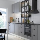 Modern kitchen with grey cabinets, black fixtures, led lights, glass shelves, stainless appliances, and large window.