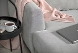 A cozy gray SLATORP sofa with a pink throw, holding a coffee cup and laptop.